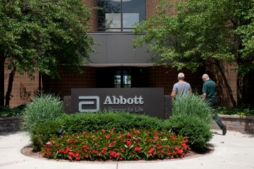 Employees walk near an Abbott Laboratories sign at the company's headquarters complex in Abbott Park, Illinois, U.S., on Monday, July 14, 2014. Abbott Laboratories said it plans to sell its generic drug business for established markets to Mylan Inc., getting in return a share of the newly combined companies in a deal valued at about $5.3 billion. Photographer: Daniel Acker/Bloomberg