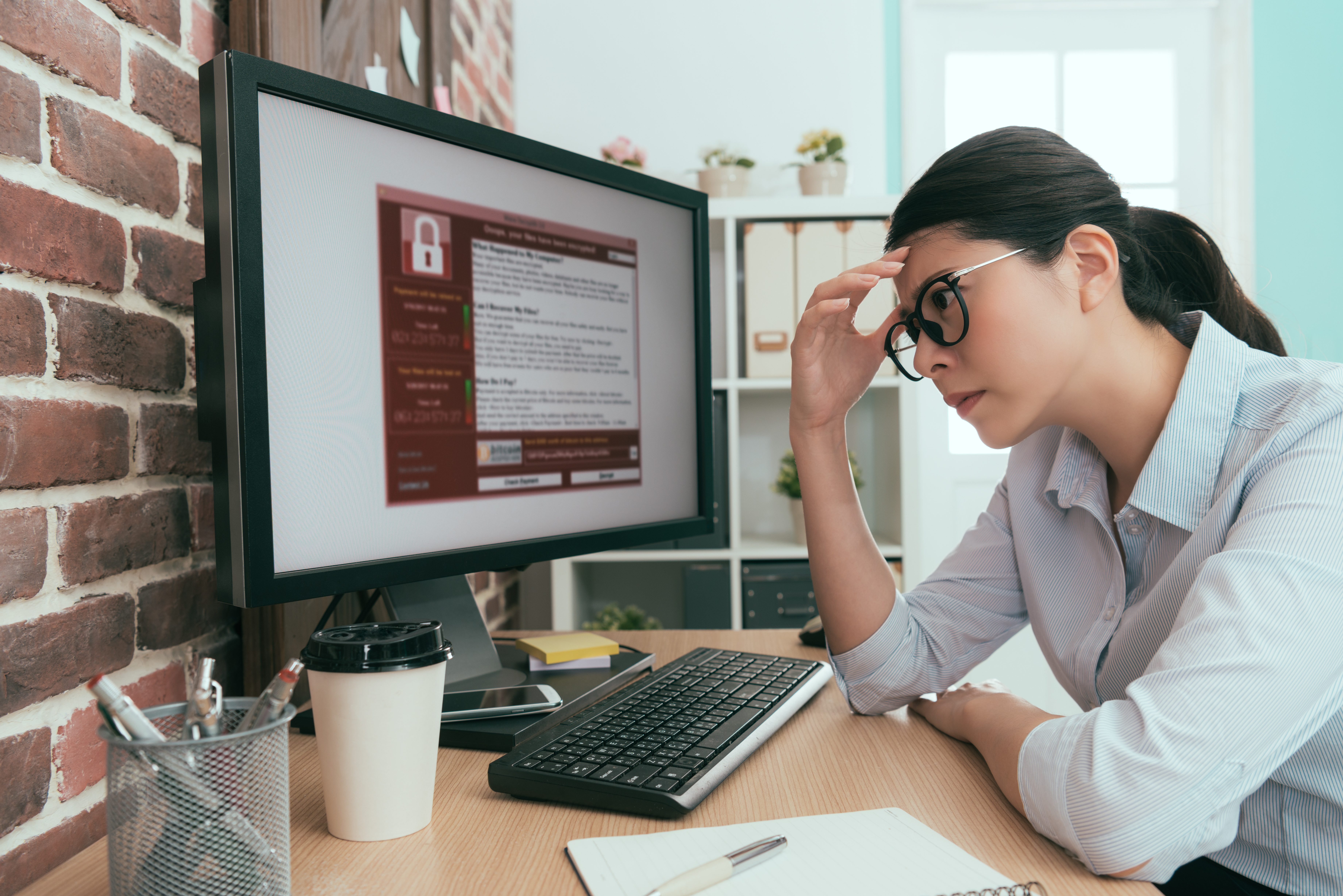 A person looks with frustration at a computer screen, which shows a dialog box with a red lock icon.