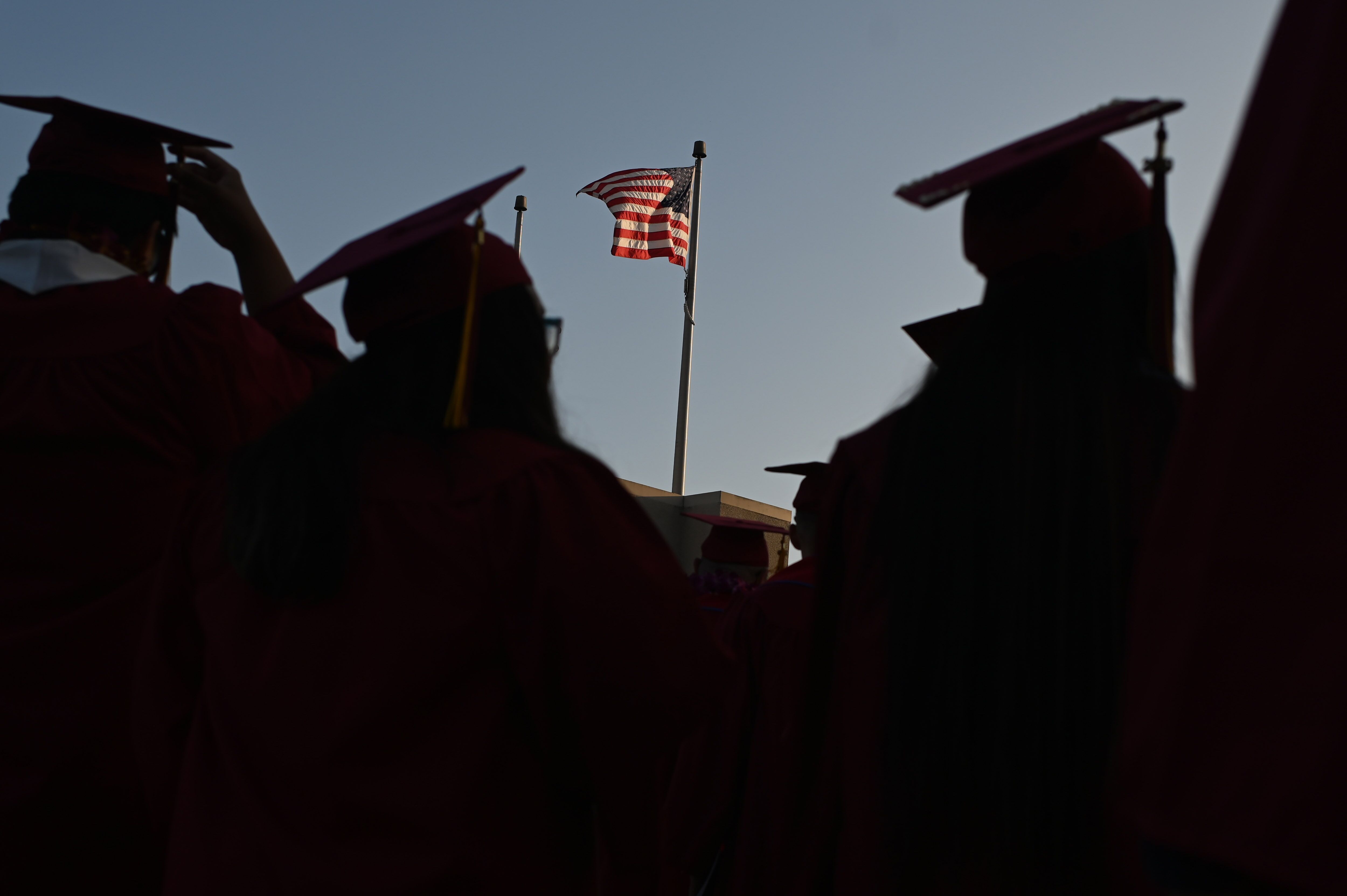 Graduates in cap and gown look on toward the American flag