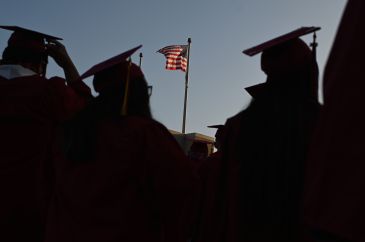 Graduates in cap and gown look on toward the American flag