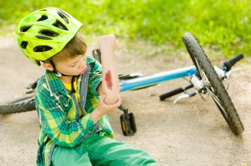Small boy wearing a helmet has a cut elbow after falling off his bike