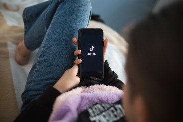 A woman holding her phone, with the app TikTok open.