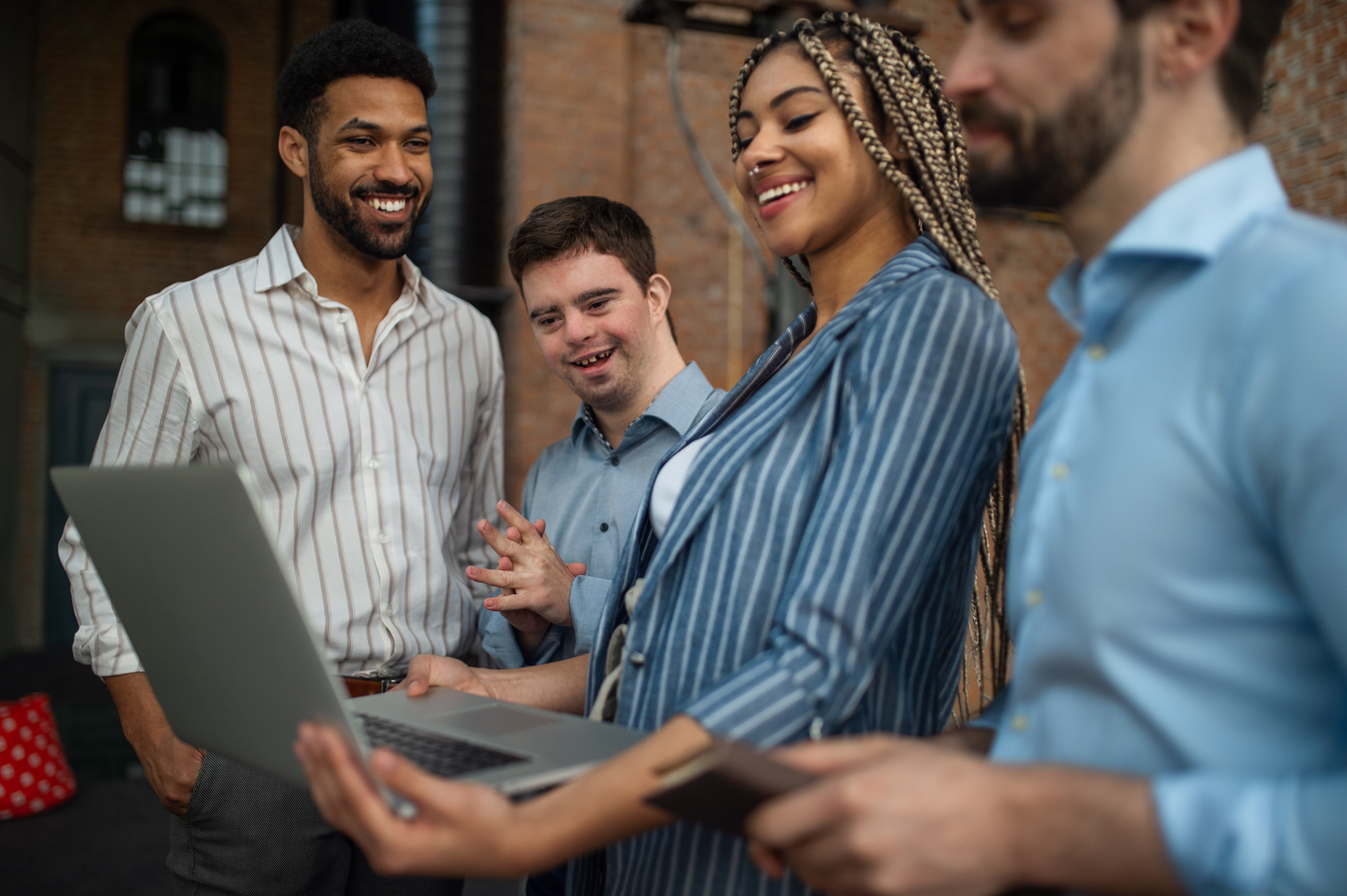 A diverse group of co-workers laughs over a laptop.