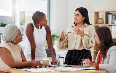A woman explains a project to her colleagues at a table.