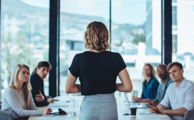 Woman standing in front of a group of people making an announcement