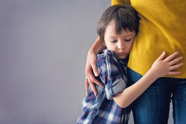 A young boy clings to his mother.