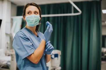 The nurse puts on gloves in a hospital room.