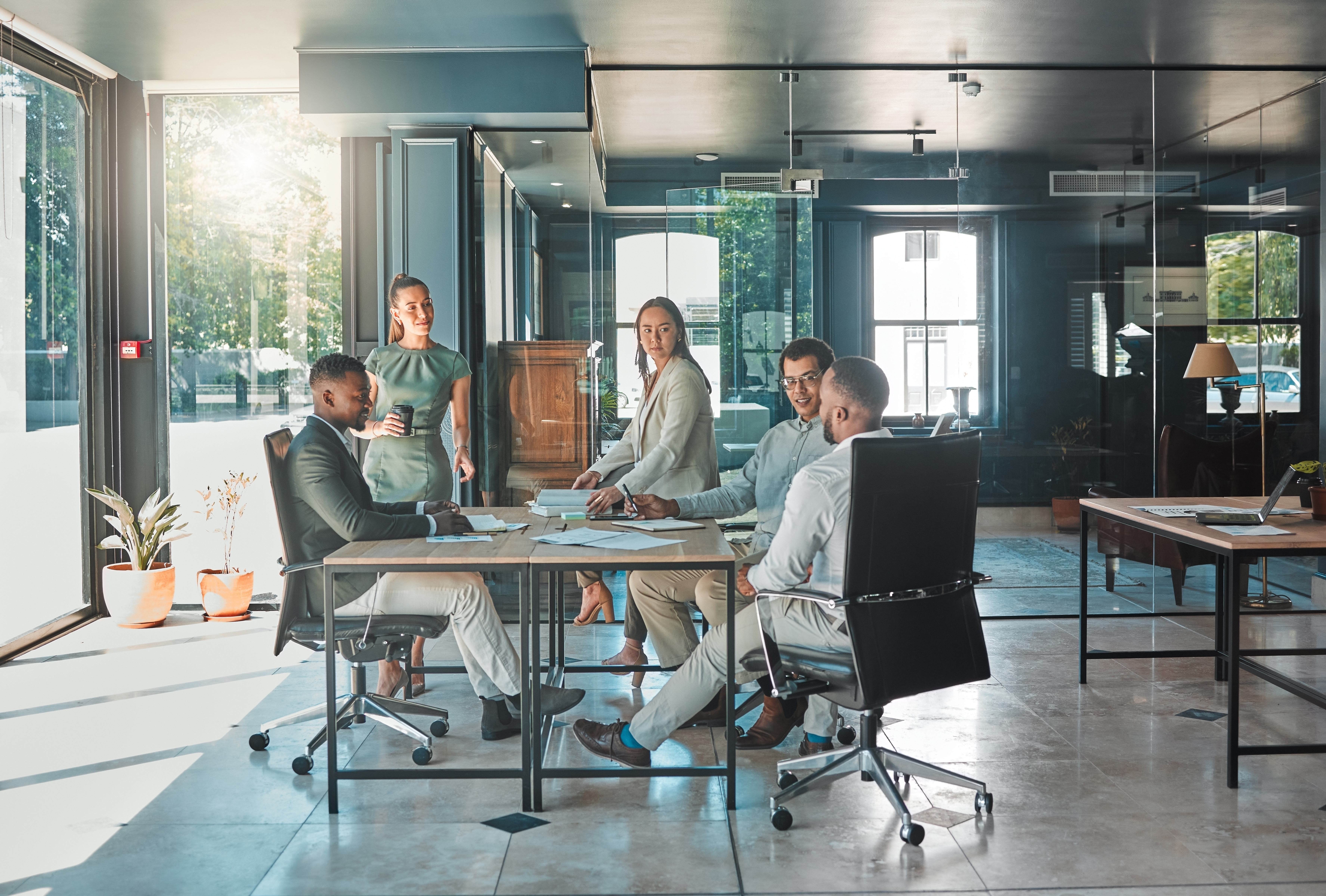 Five workers speak to each other at a conference table.