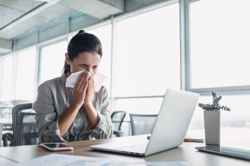 Woman blowing her nose sitting at a work desk