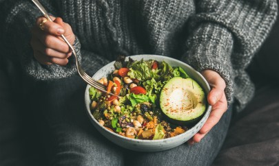 A woman holds a bowl of salad in her lap.