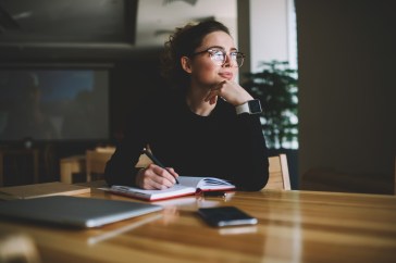 A woman is writing in her notebook, deep in thought.
