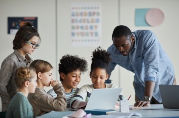 Teacher helps young students as they look at a tablet.