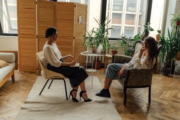 A female therapist and female patient sit facing each other in chairs in an office filled with plants