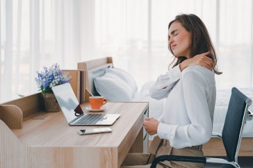 A young woman rubs her neck in pain at her desk.