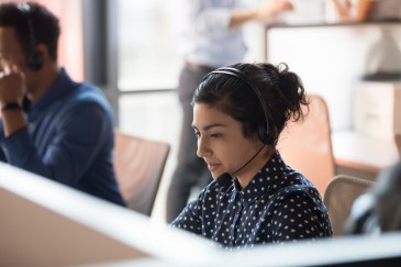 A call center agent wears a headset at their desk.