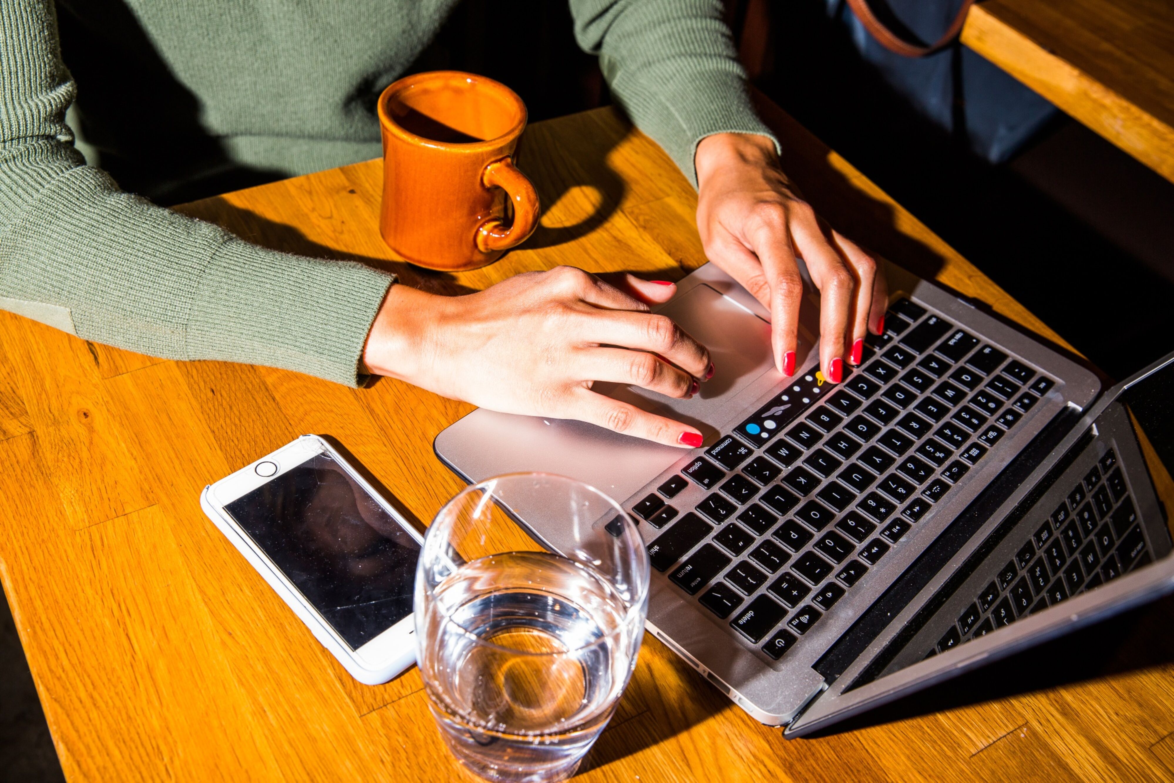 Woman with red manicure typing on a laptop with a glass of water on her desk.