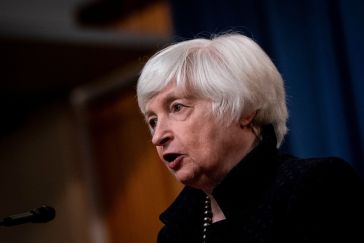 U.S. Treasury Secretary Janet Yellen speaking into a microphone, the background is blurred.