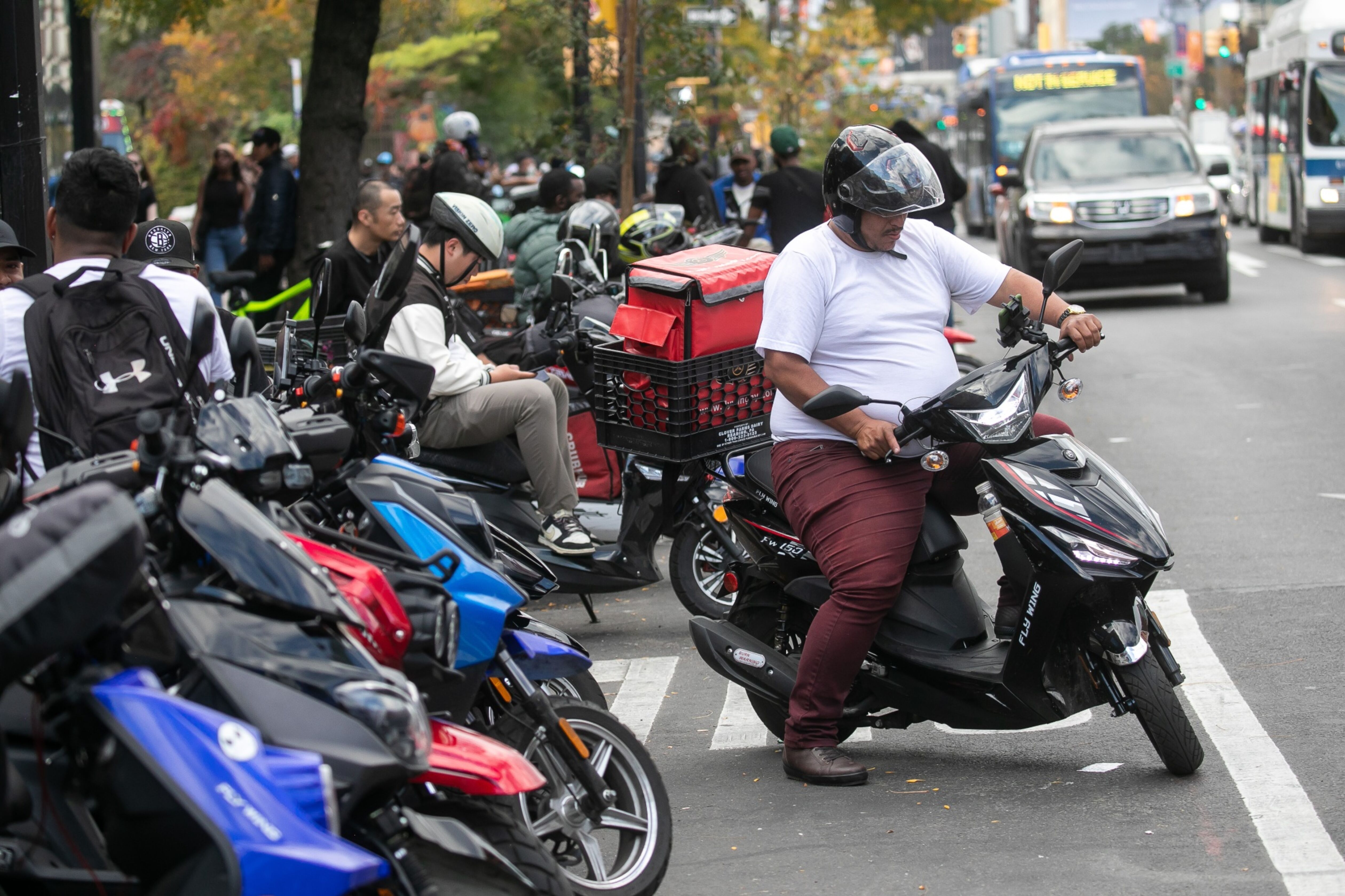 A row of electronic bikes and scooters line New York streets, with drivers waiting to accept delivery order assignments.