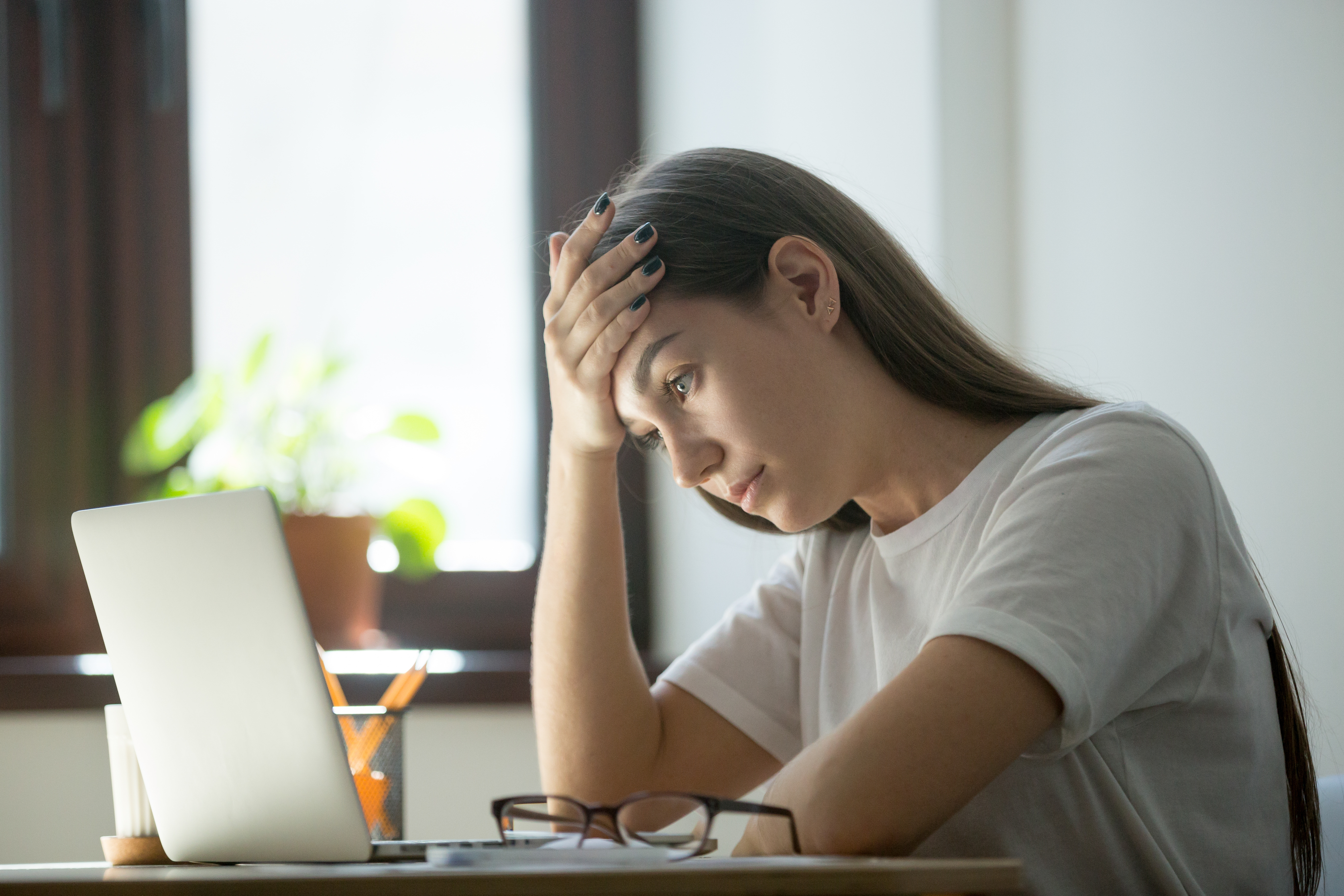 A woman looks at her laptop with a pained worried expression.
