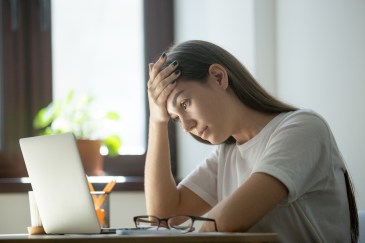 A woman looks at her laptop with a pained worried expression.