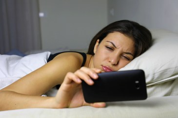 Woman looking at her phone while lying in bed