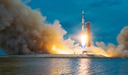 A rocket takes off into a dark blue sky, smoke flying around it.