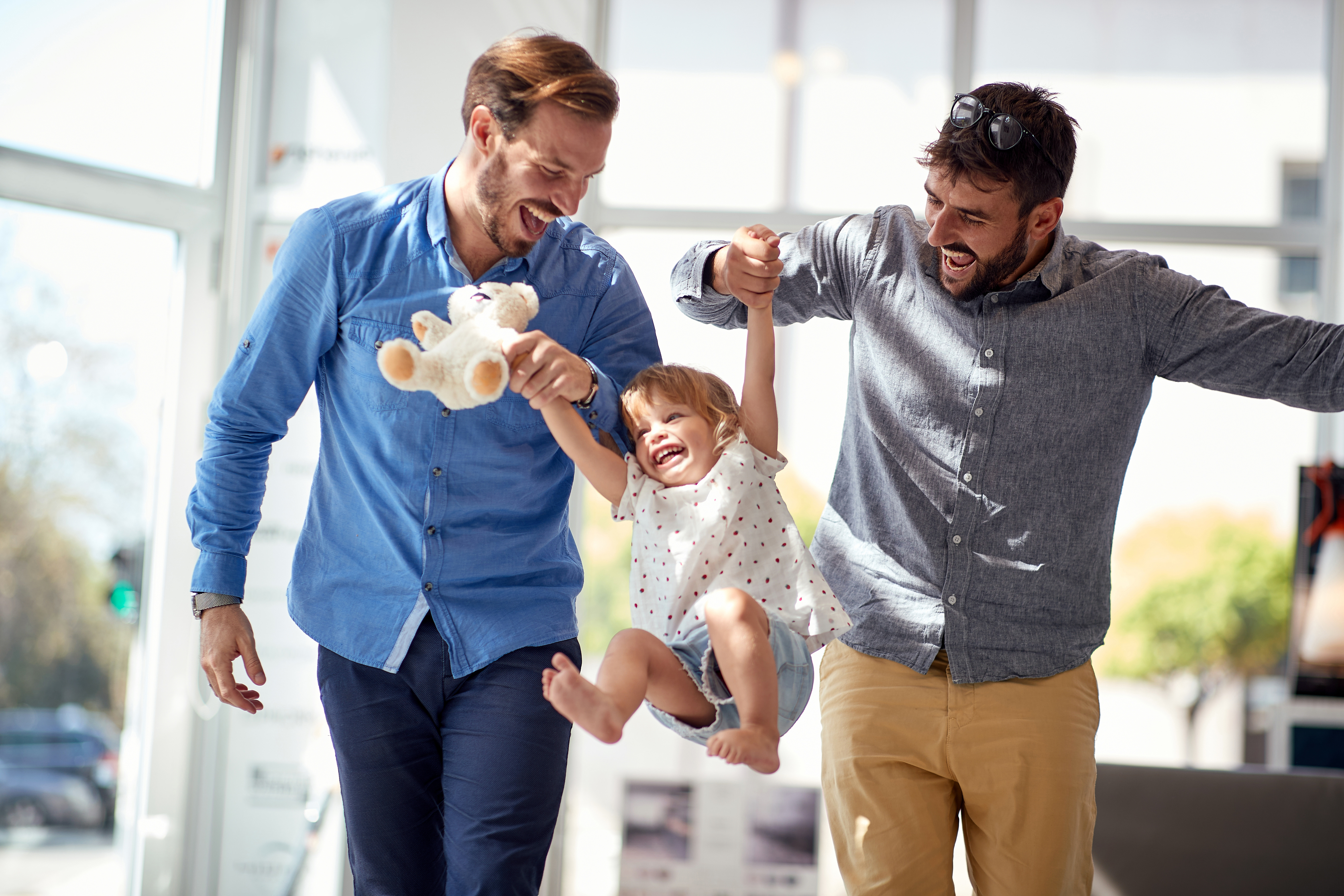 Two dads swing their daughter in the air while laughing