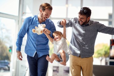 Two dads swing their daughter in the air while laughing
