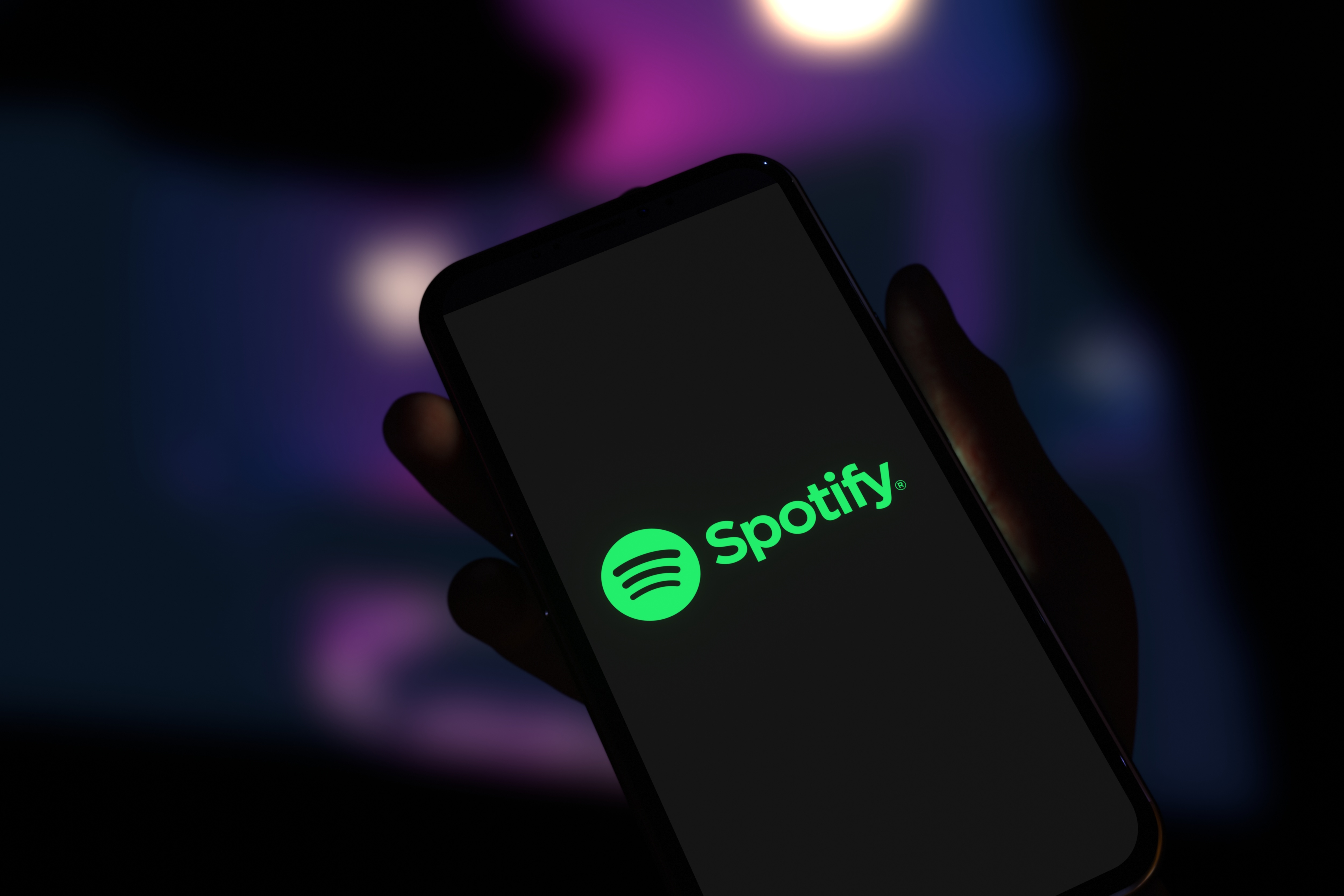 Hand holding a cell phone with the Spotify logo on the screen