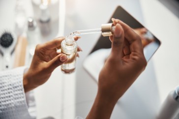 A black woman opens a bottle of skin vitamin serum.
