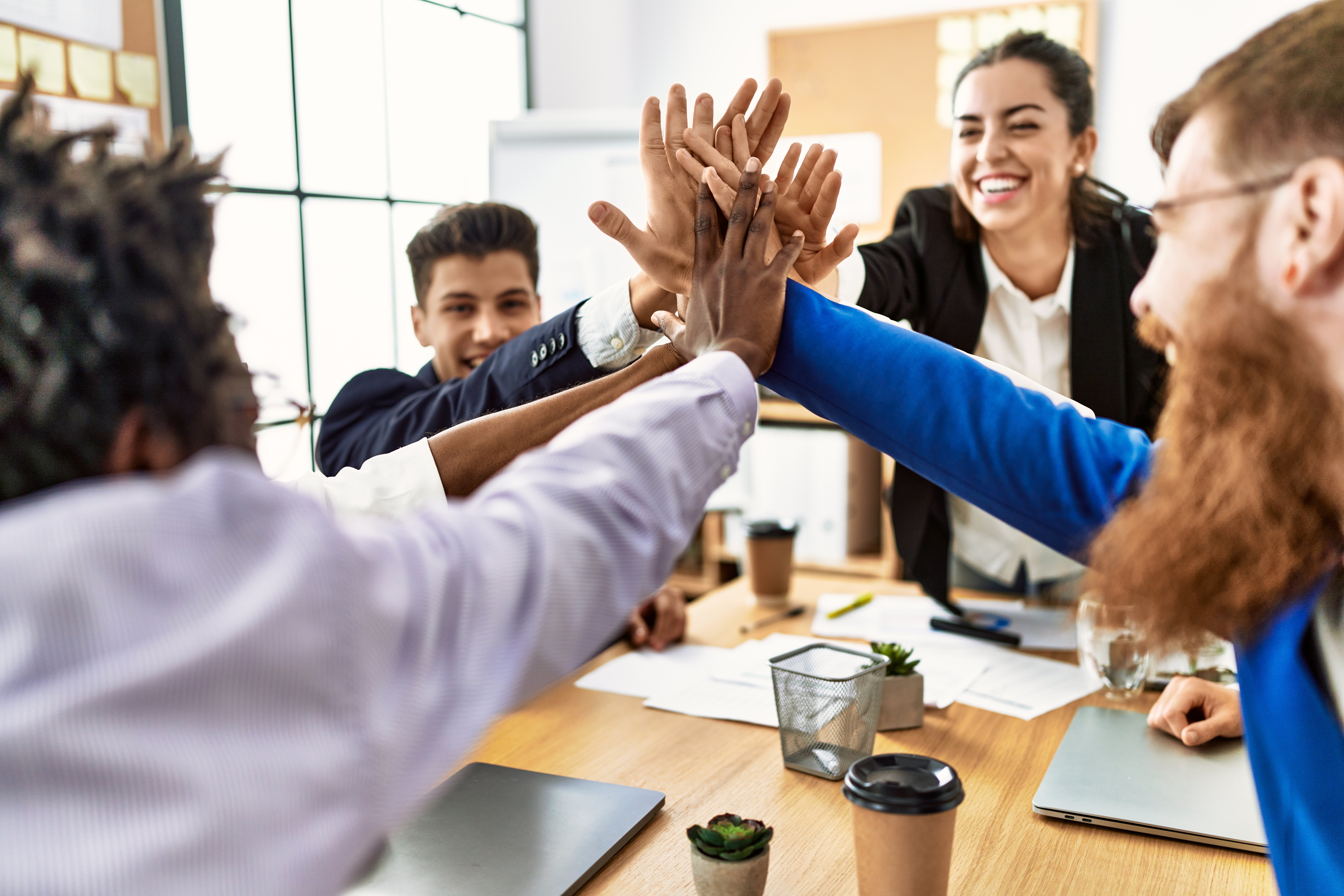 Five coworkers high-five each other over a worktable