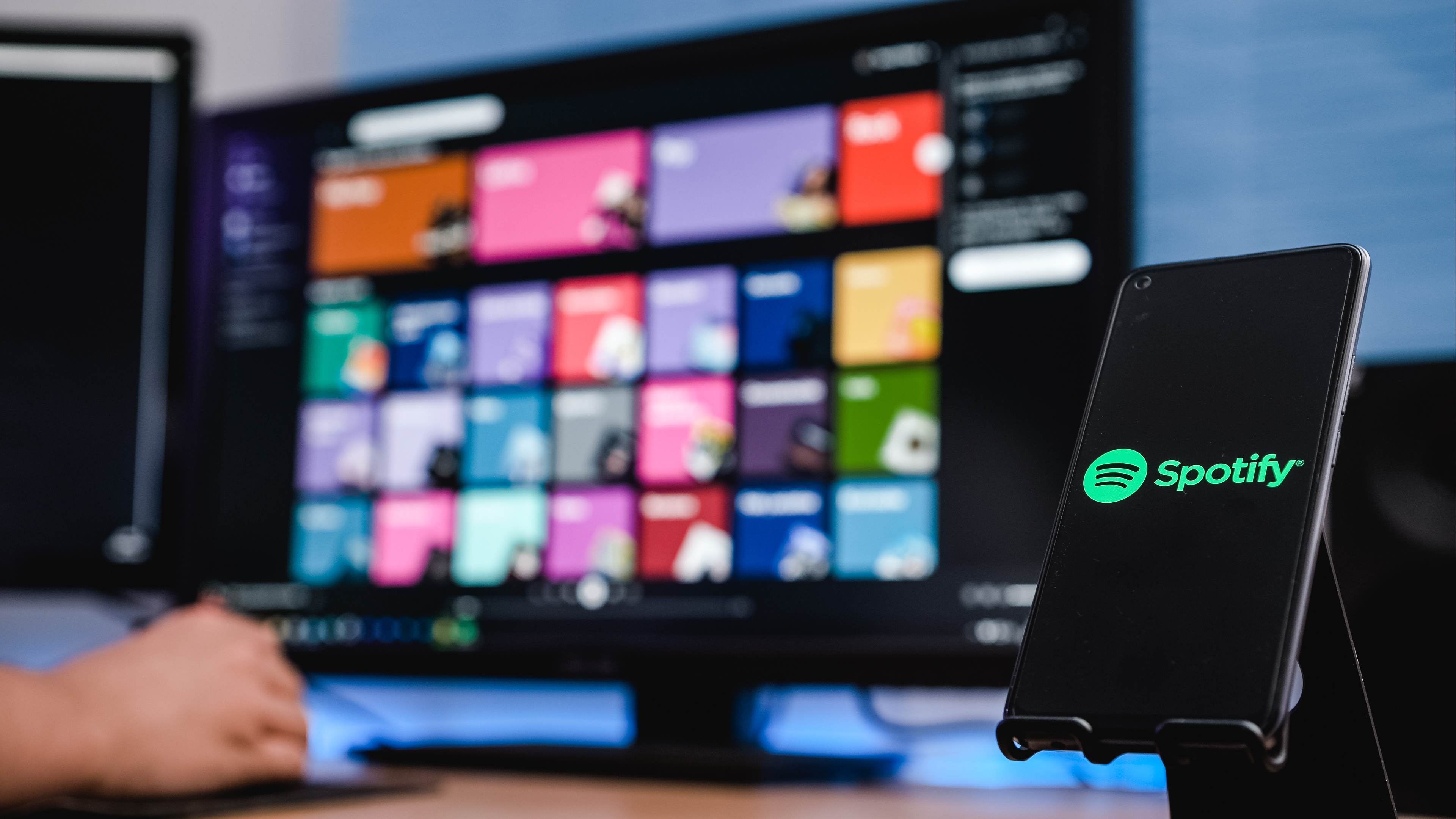 Spotify logo with music playlists in the background on a computer screen.