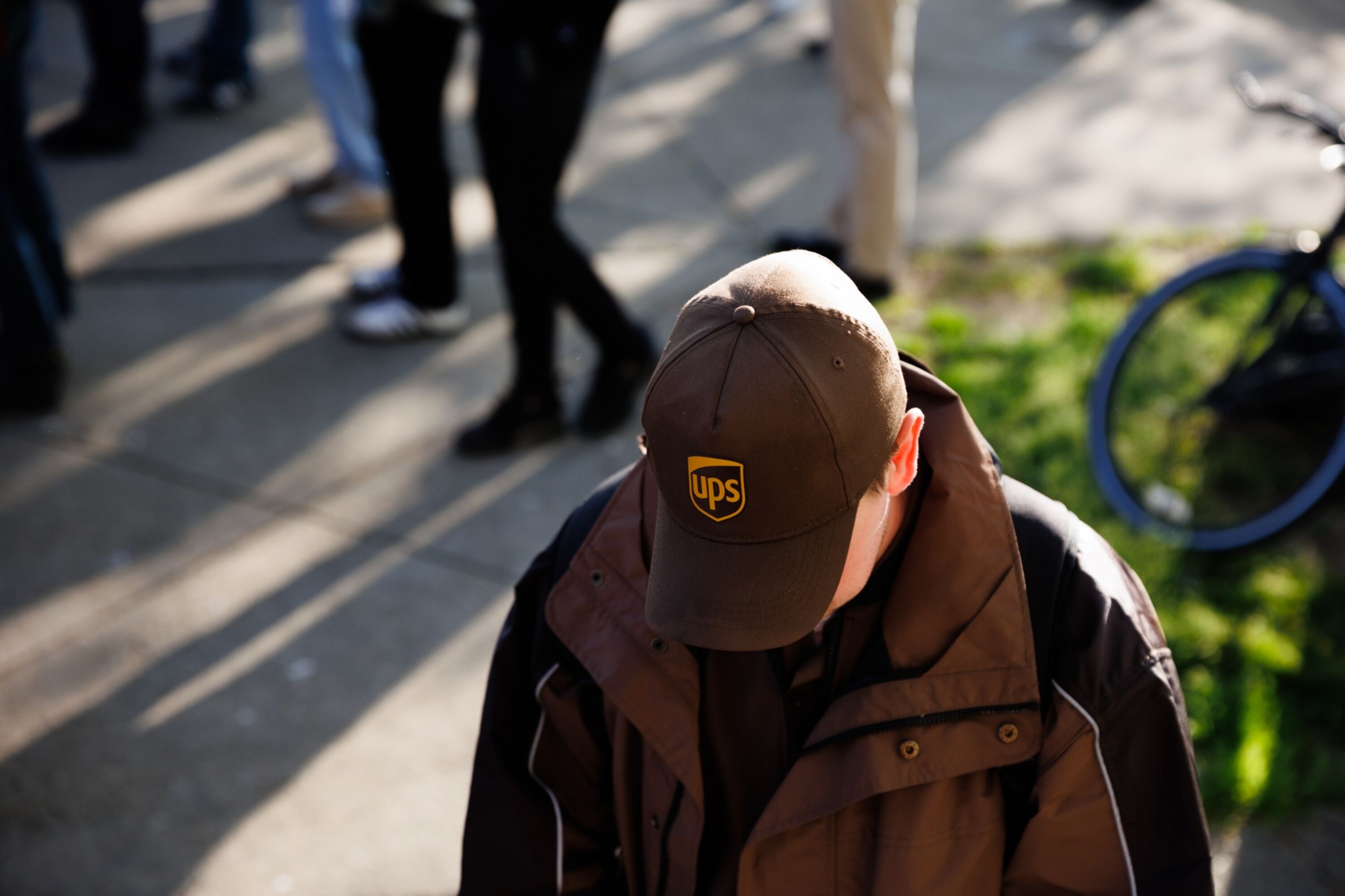 A man in a UPS cap with his head down, a busy street in the background.