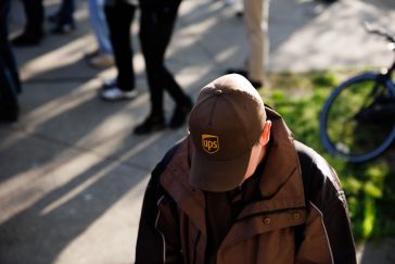 A man in a UPS cap with his head down, a busy street in the background.
