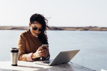 Woman working outside with phone and computer
