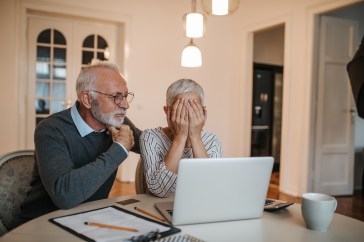 Older man and woman sitting in front of their computer as the woman covers her eyes