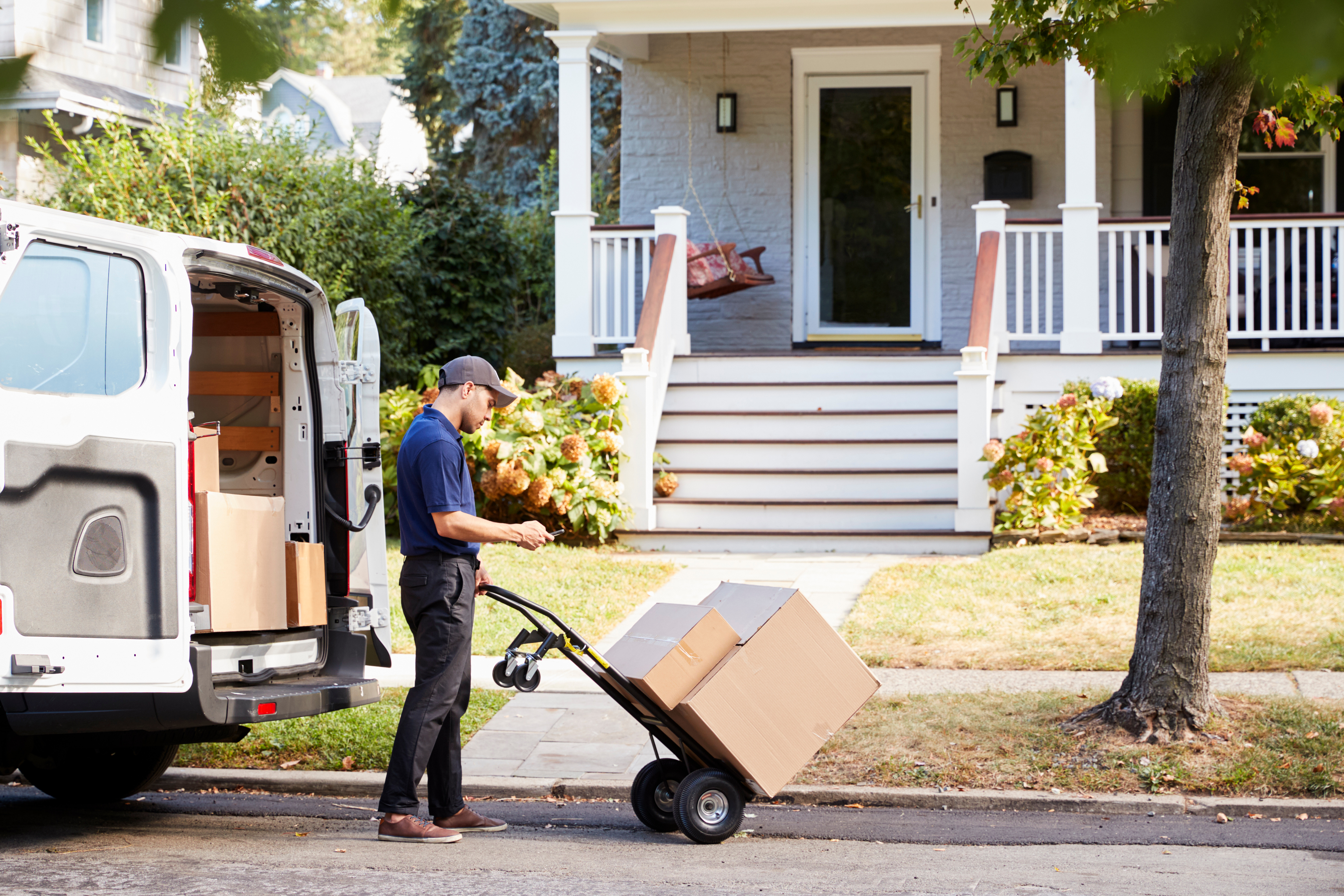 The delivery man uses a dolly to bring two packages to the front door.