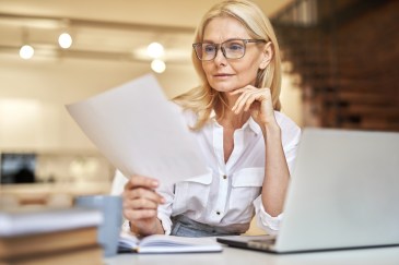 Female employee with laptop reading paper