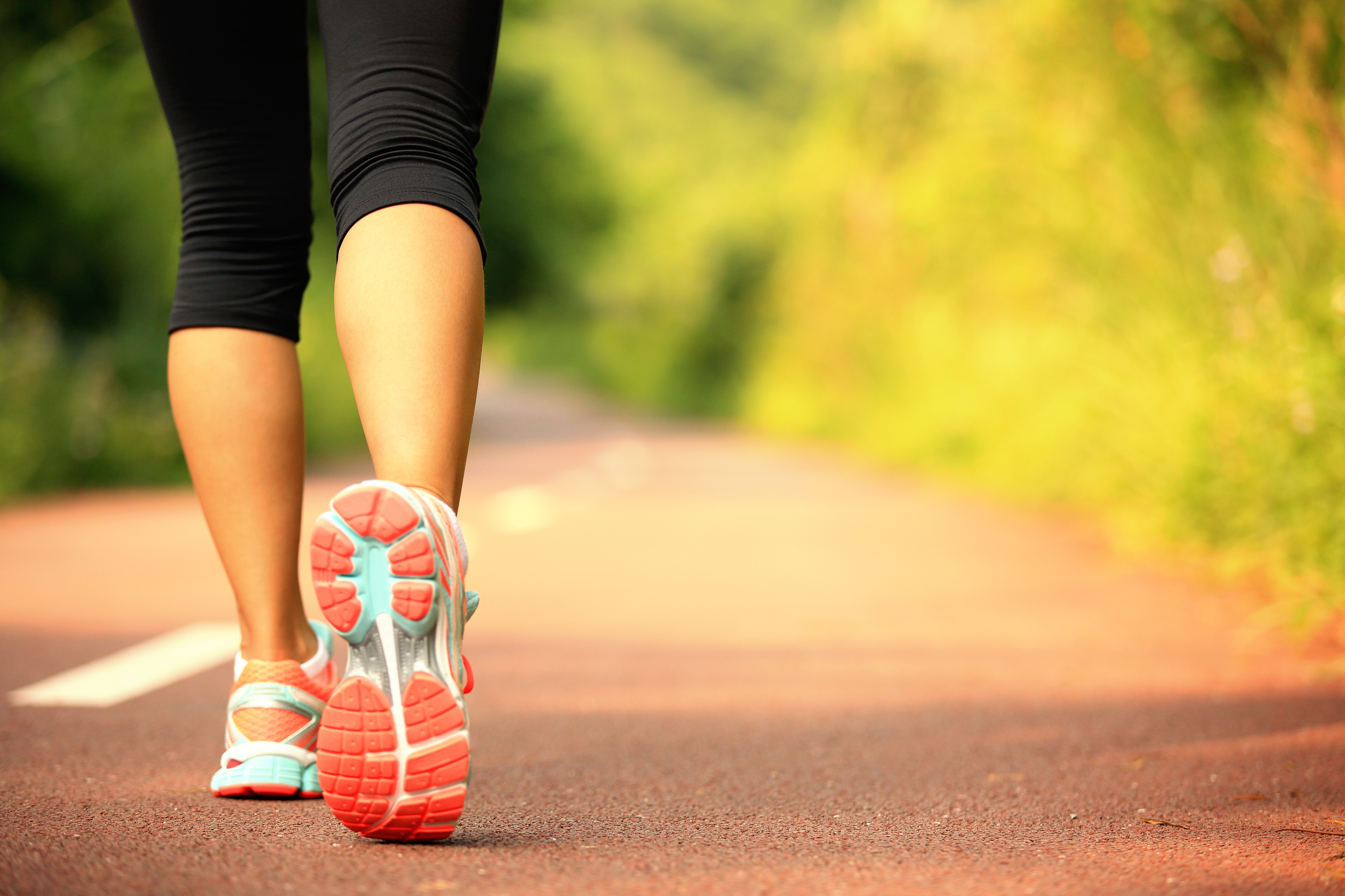 A lady is walking on a bike path; the focus is on the foot that's lifted, showing the bottom of her orange and blue sneaker.