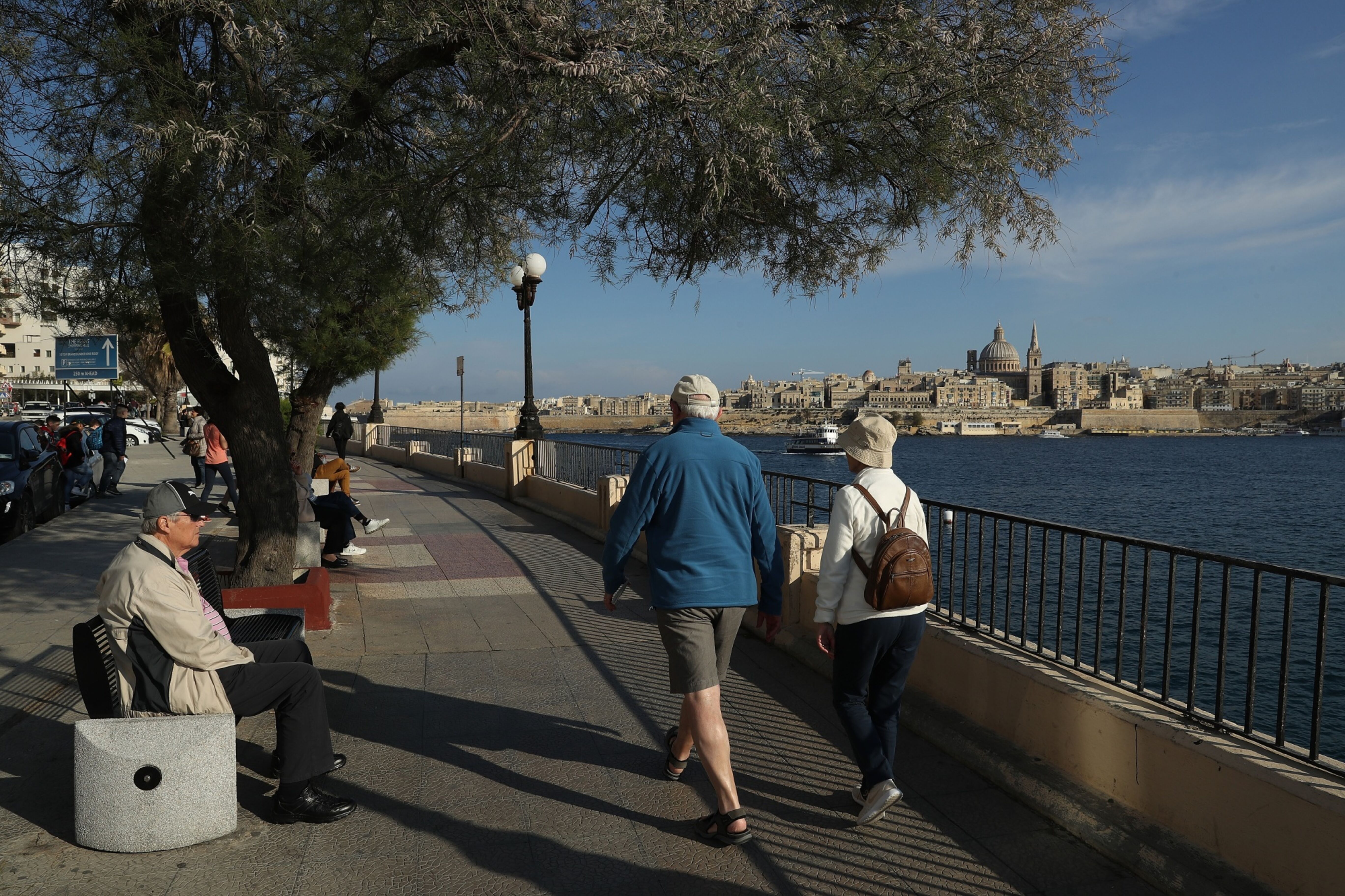 Older man and woman walking along the river with a city skyline in the background