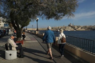 Older man and woman walking along the river with a city skyline in the background