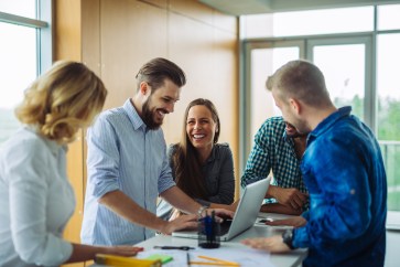Group of adults standing around a computer smiling