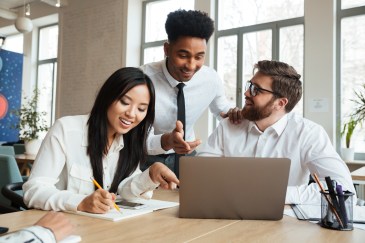 A group of employees gathering around a computer and smiling.