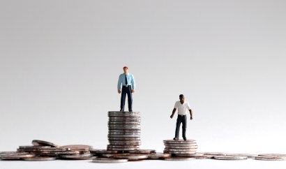 A figurine of a white businessman standing on a stack of quarters, next to a shorter stack of quarters with a black figurine on top