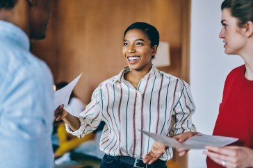 Female employee handing paper to another employee, smiling