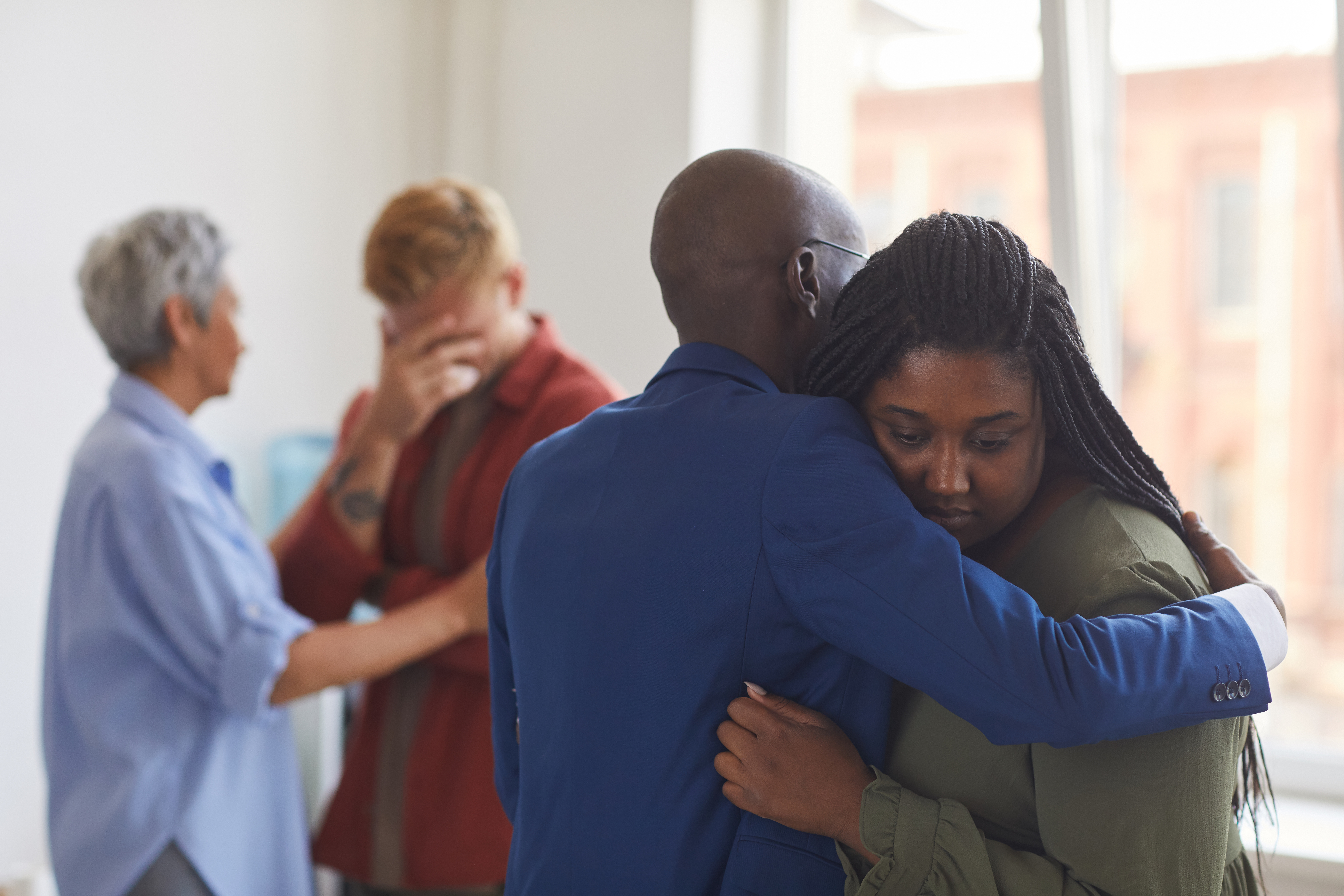 Man hugging a woman who looks upset, while another woman comforts a man in the background