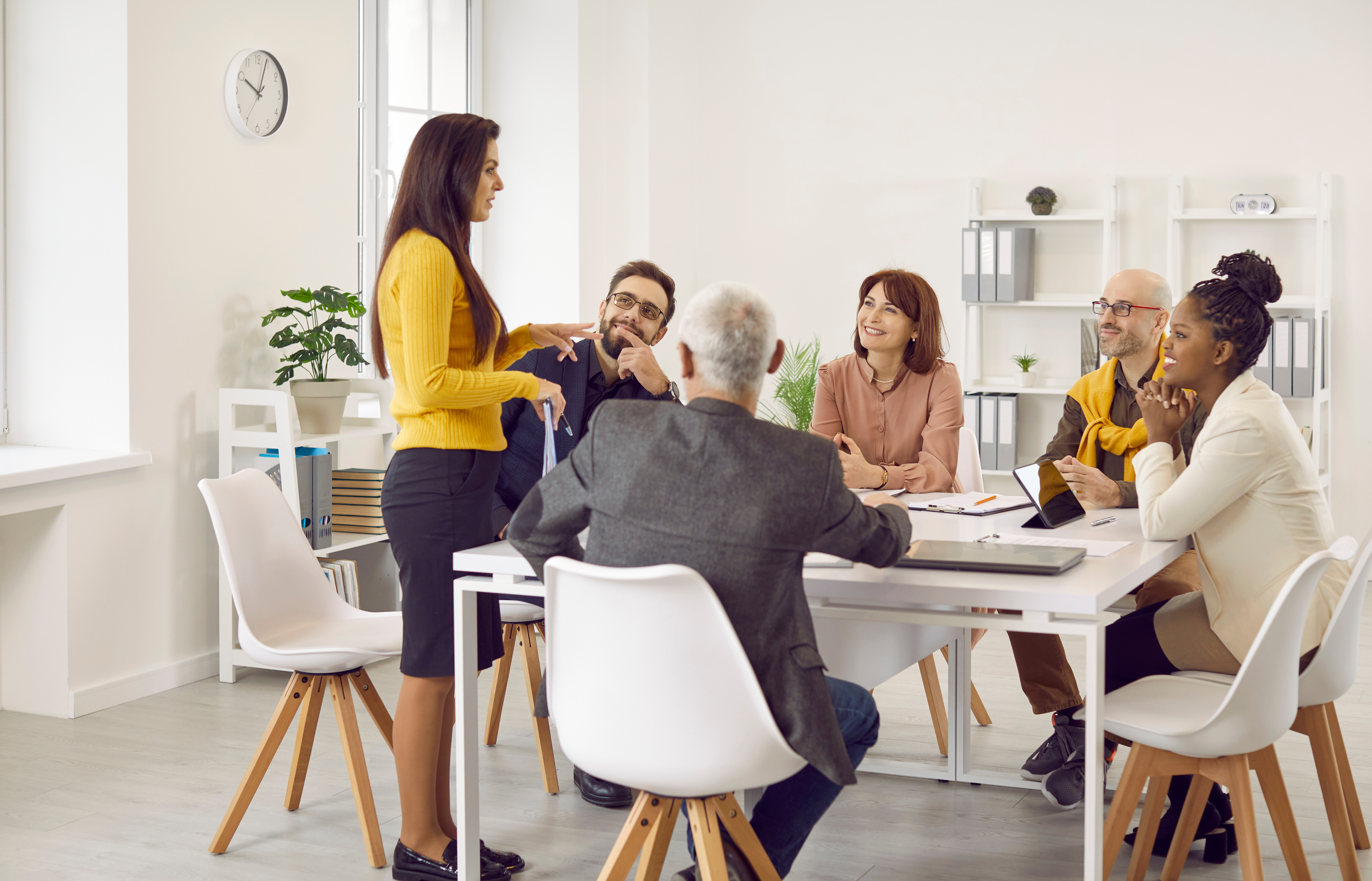 Group of employees meeting around a table, one female employee standing and speaking
