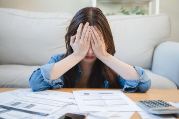 Woman with her head in her hands sitting in front of a table with bills and a calculator