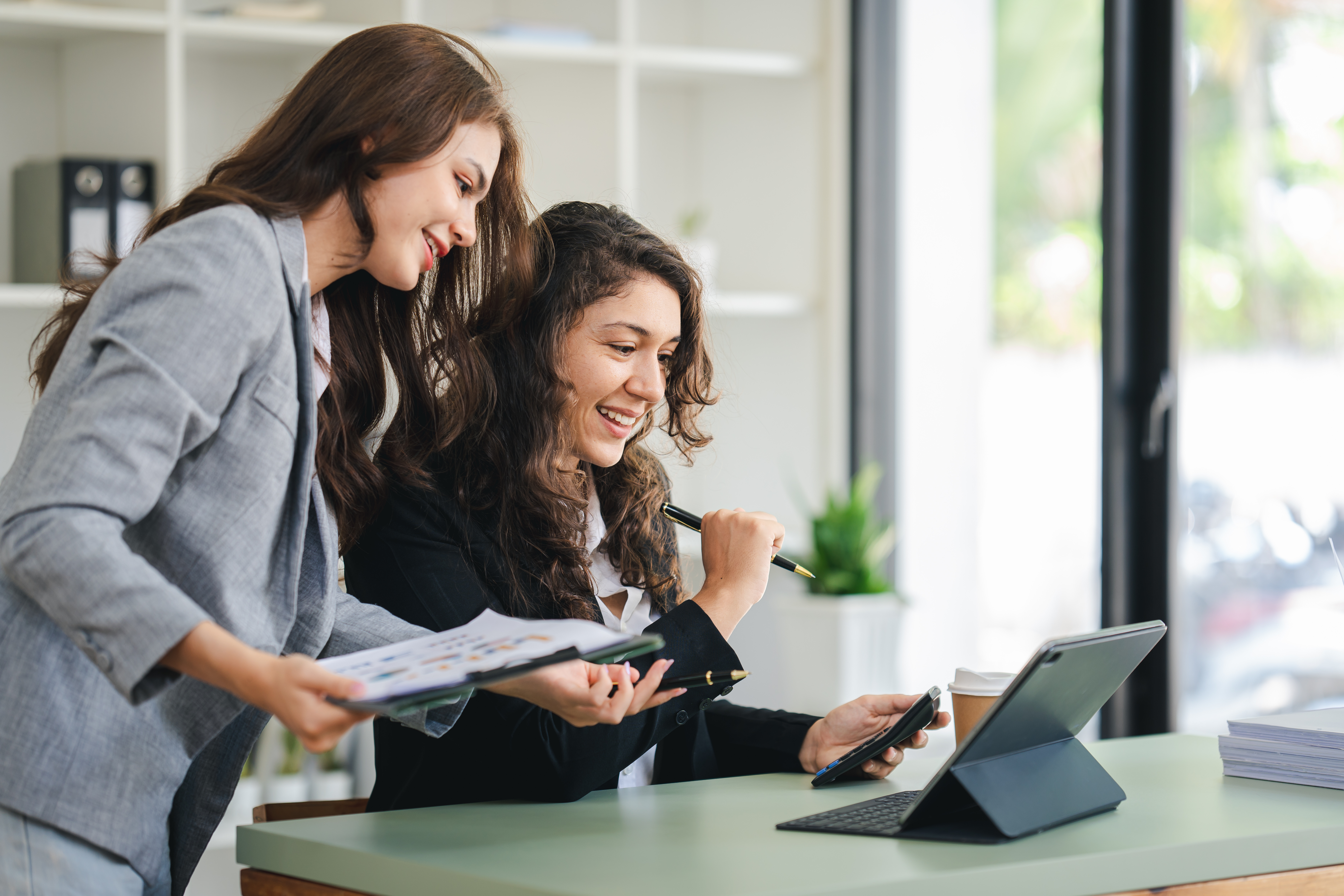 Female employees working together, one sitting with computer, one standing