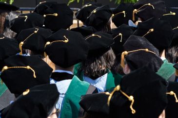 A sea of graduates at a graduation ceremony pictured from behind so their caps show.
